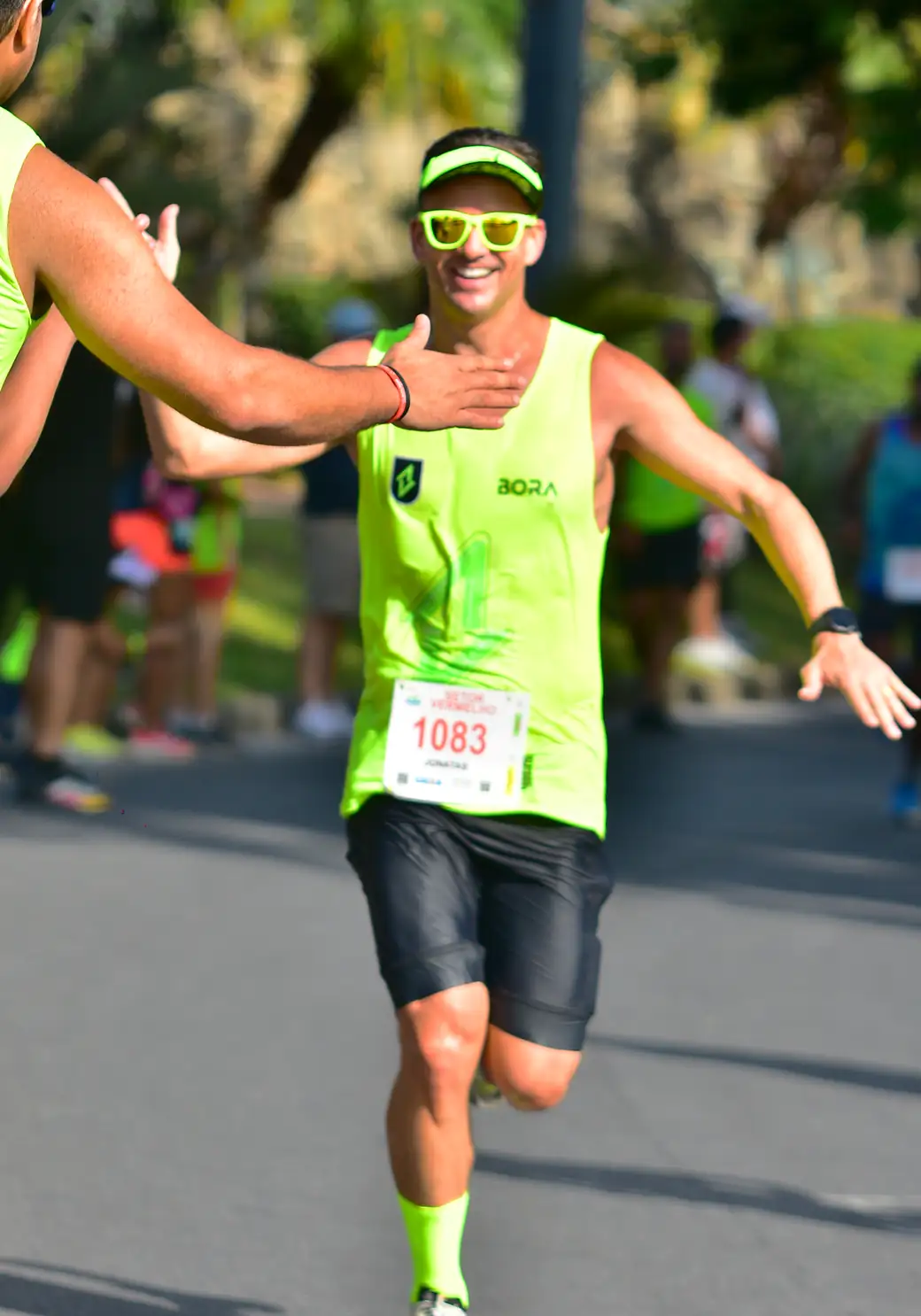 A BORA athlete running with both arms wide open, in the neon green kit